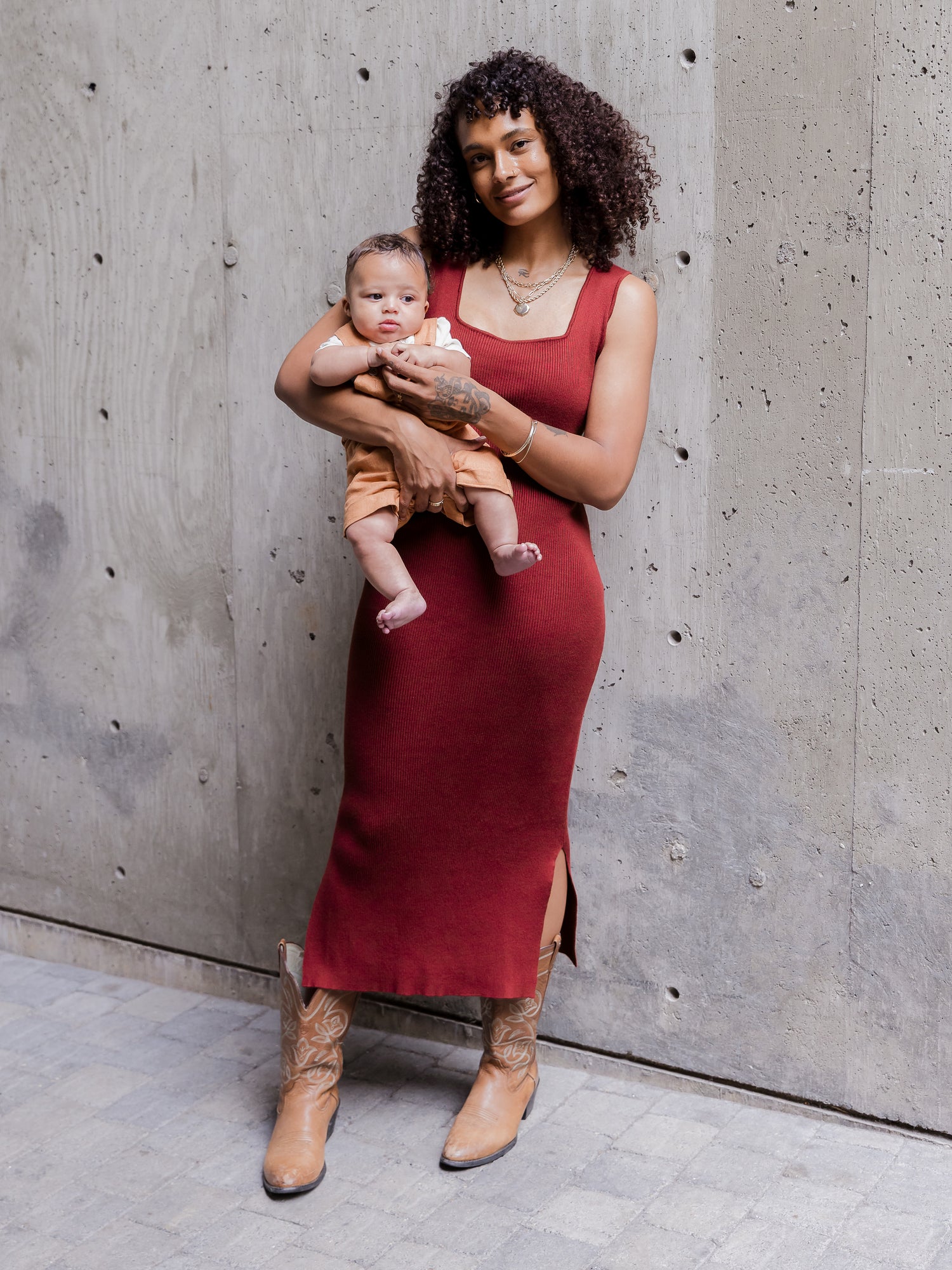 Front view of model wearing the 2-in-1 Maternity & Nursing Midi Dress in Garnet without the top long-sleeve cropped layer, holding baby