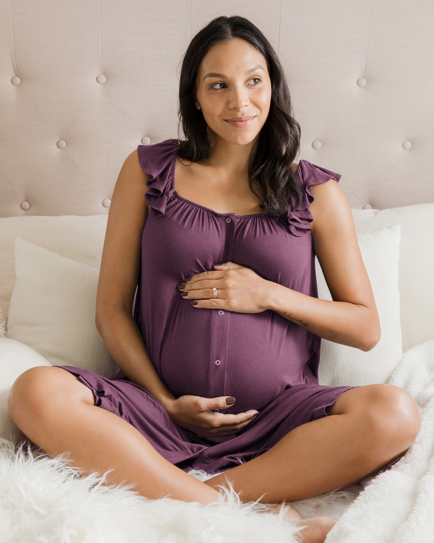 Pregnant model sitting on bed wearing the Ruffle Strap Labor & Delivery Gown in Burgundy Plum