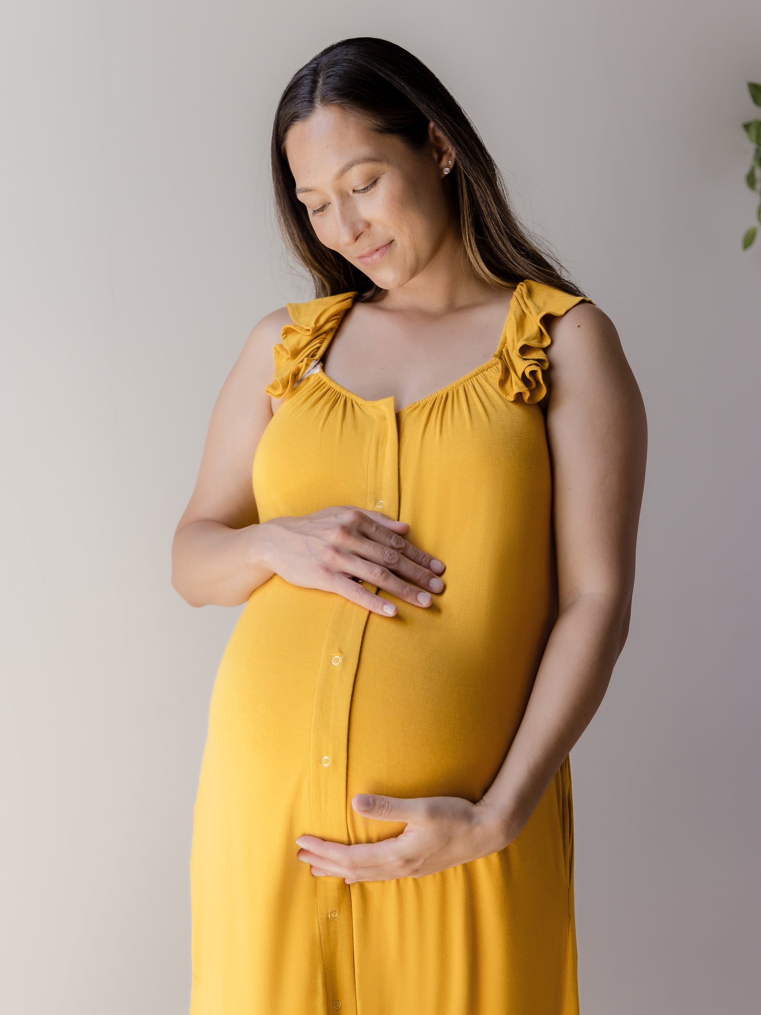 Cropped in front view of pregnant model wearing the Ruffle Strap Labor & Delivery Gown in Honey. 