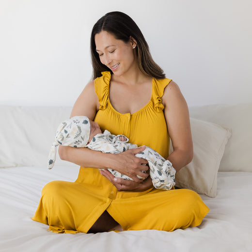 Model wearing the Ruffle Strap Labor & Delivery Gown in Honey holding baby wearing the Baby Knotted Gown & Hat Set in Honey Dandelion.