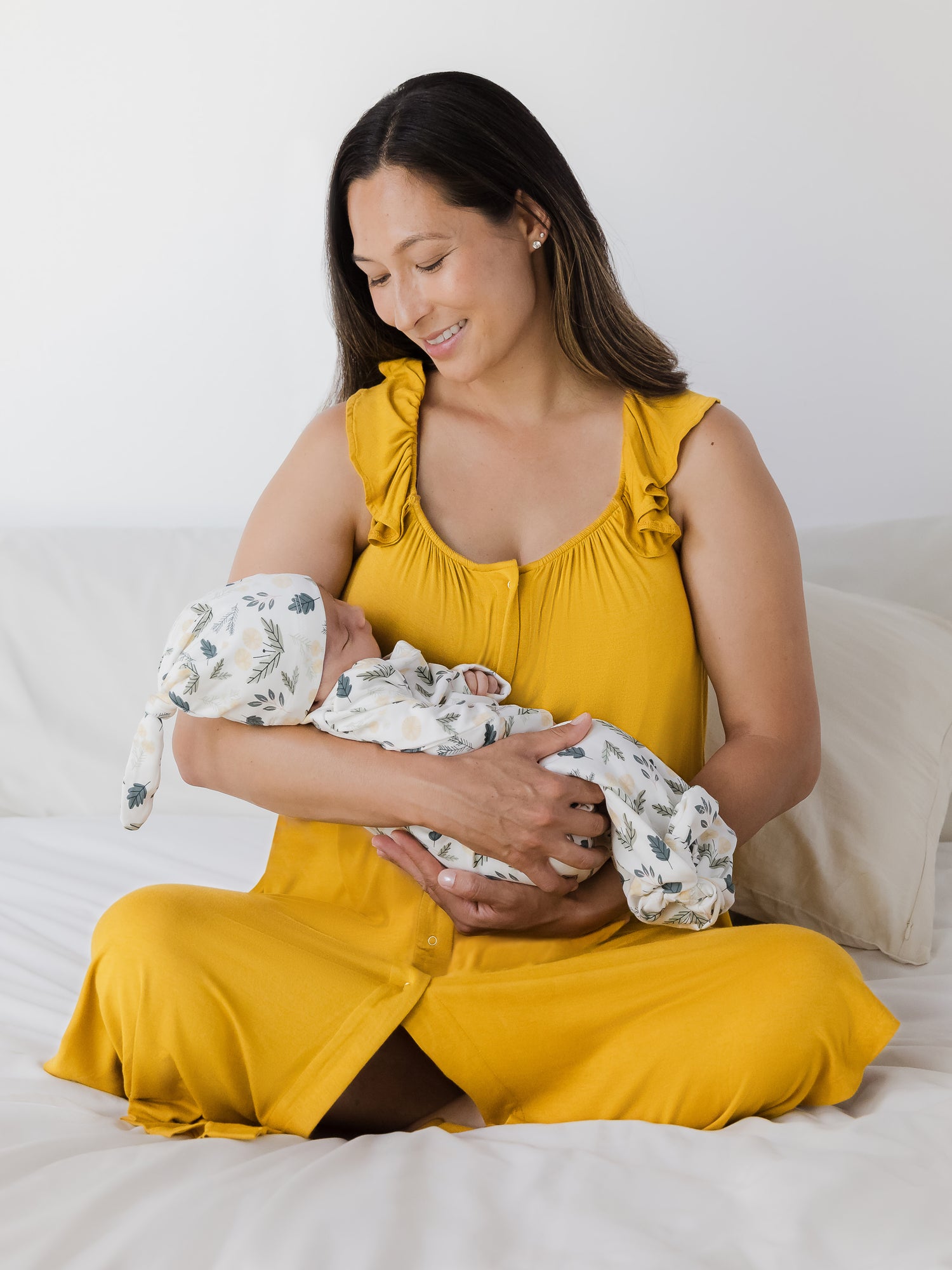 Model wearing the Ruffle Strap Labor & Delivery Gown in Honey holding baby wearing the Baby Knotted Gown & Hat Set in Honey Dandelion.