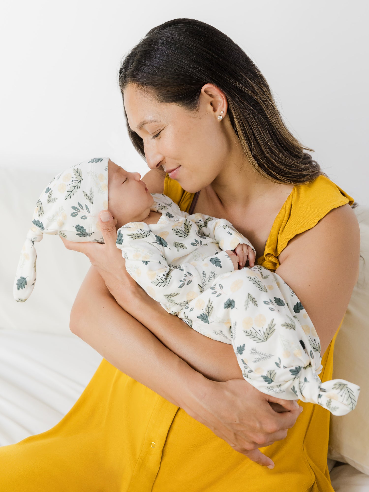 Model holding newborn who is wearing the Baby Knotted Gown & Hat Set in Honey Dandelion.