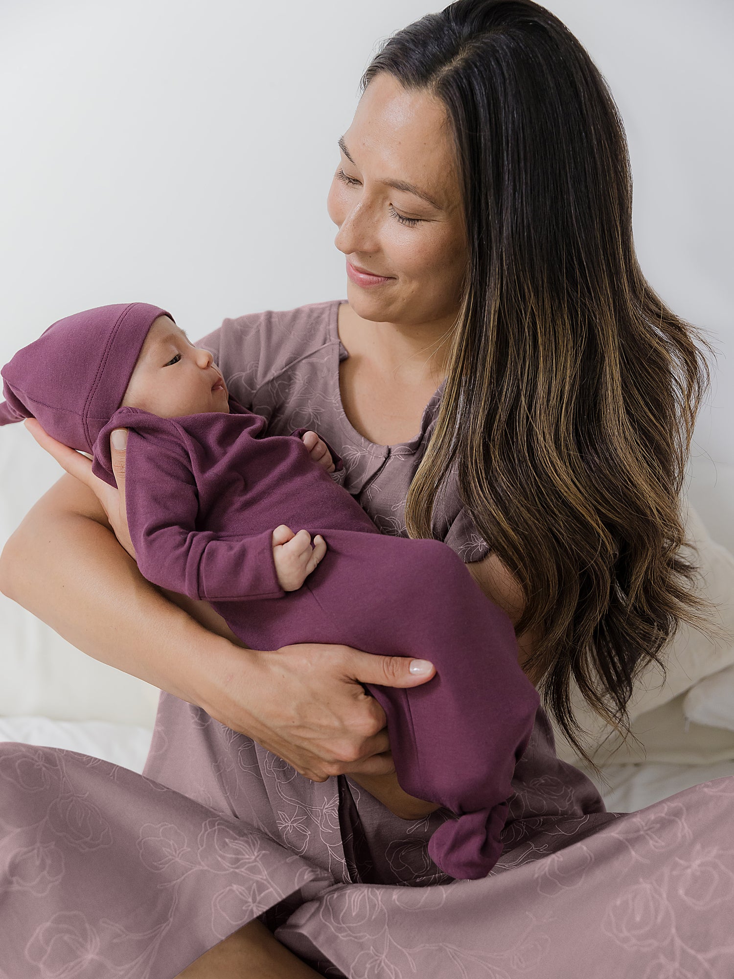 Baby wearing the Baby Knotted Gown & Hat Set in Burgundy Plum being cradled by mom.