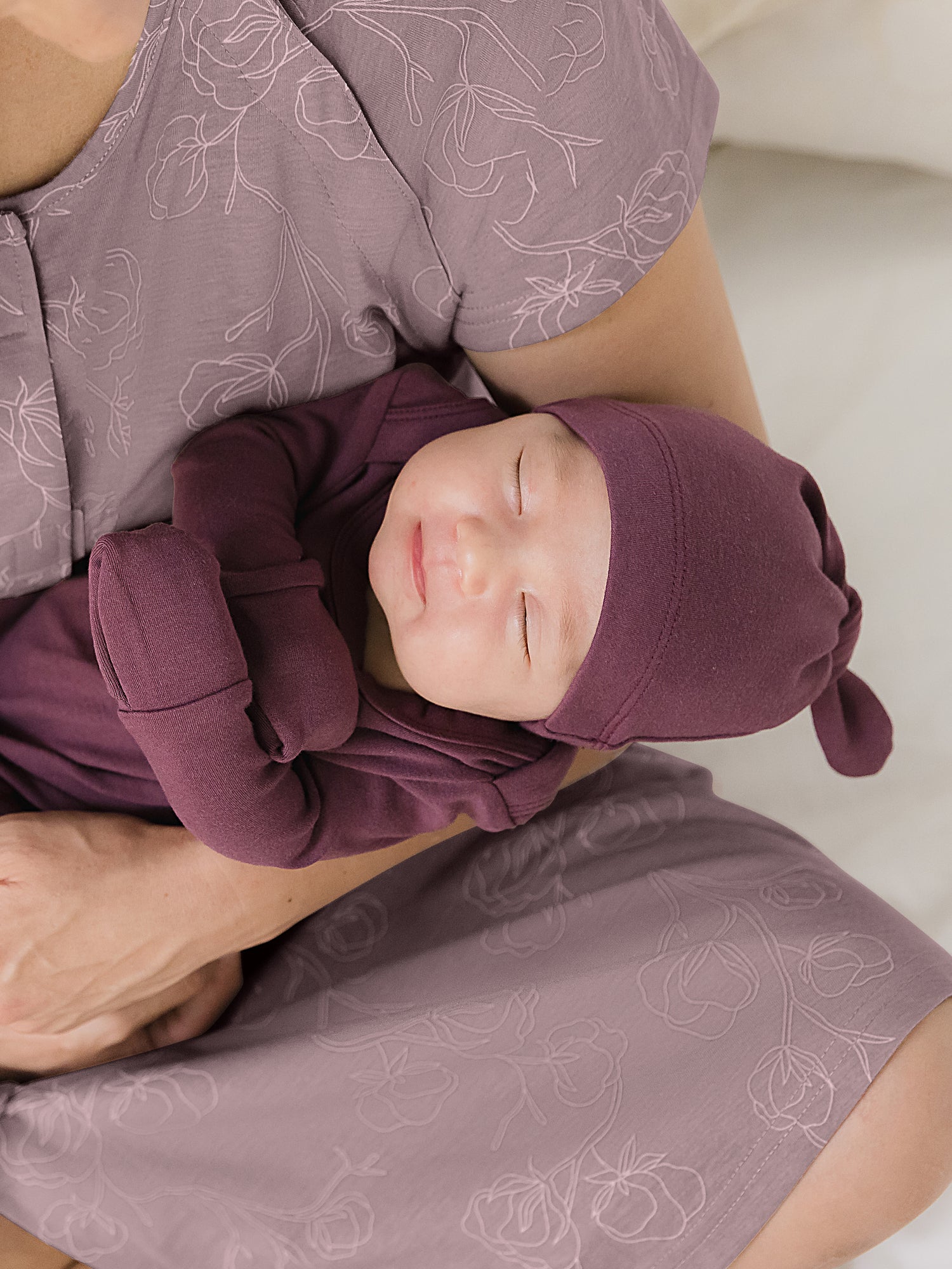 Close up of baby wearing the Baby Knotted Gown & Hat Set in Burgundy Plum with cuffs over hands, being held by mom.