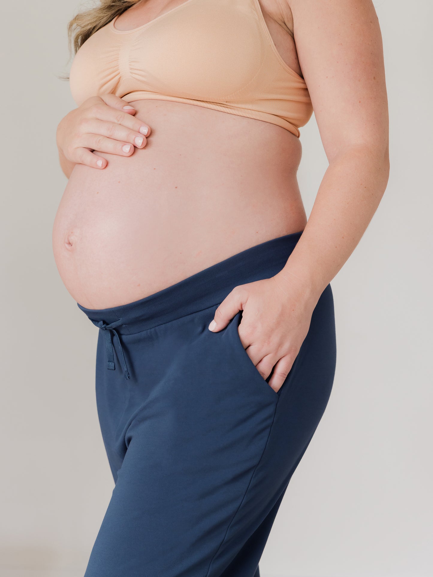 Close up side view of pregnant model wearing the Bamboo Maternity & Postpartum Jogger in Navy, with one hand in a pocket@model_info:Erin is wearing a Medium.