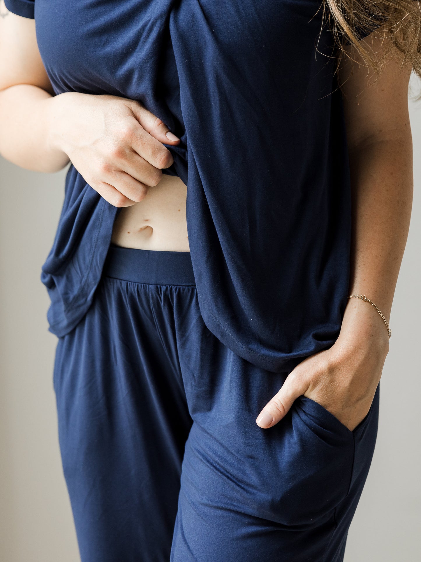 Cropped in image of model wearing a Short Sleeve Tulip Hem Maternity Pajama set - Top & Bottom in Navy Blue, showing waistband, with one hand in pocket.
