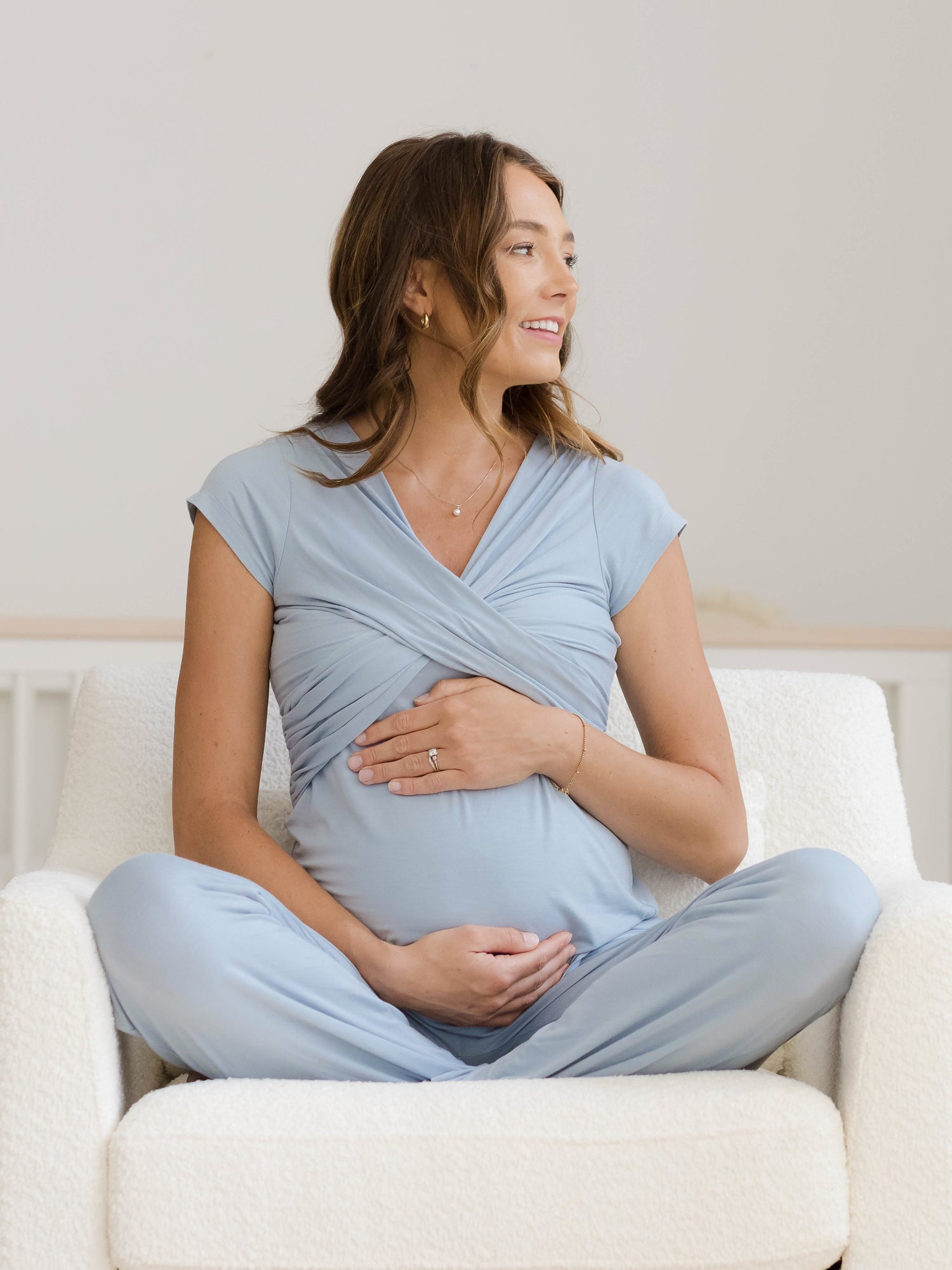 Pregnant model sitting cross-legged on chair wearing the Davy Maternity & Nursing Pajama Set in Mist. @model_info:Kate is wearing a Small.