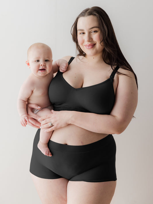 Model holding baby and wearing the Black Grow with Me™ Maternity & Postpartum Boyshort in black@model_info:Rachel is wearing an X-Large.