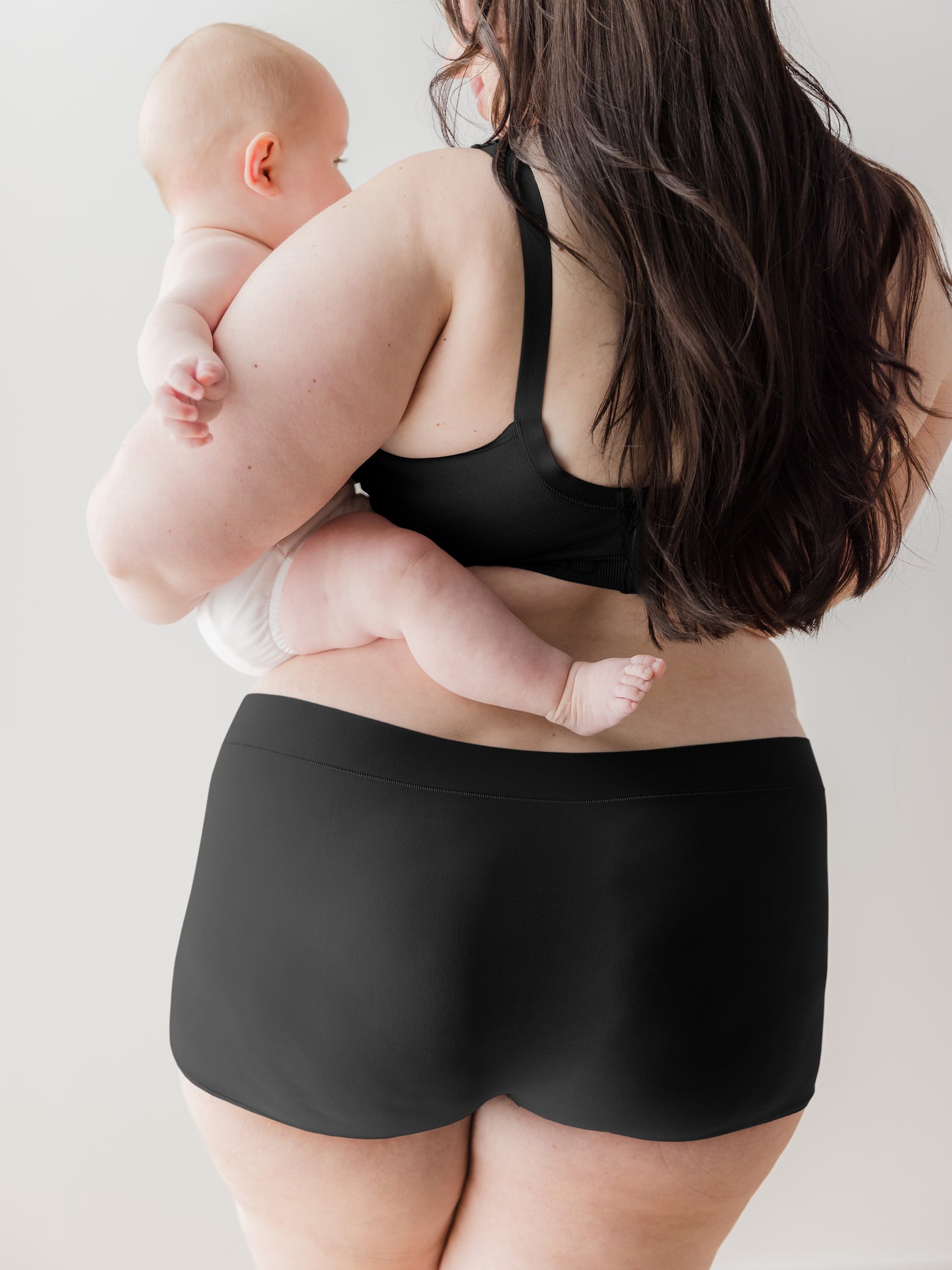 Back view of model holding baby and wearing the Black Grow with Me™ Maternity & Postpartum Boyshort in black