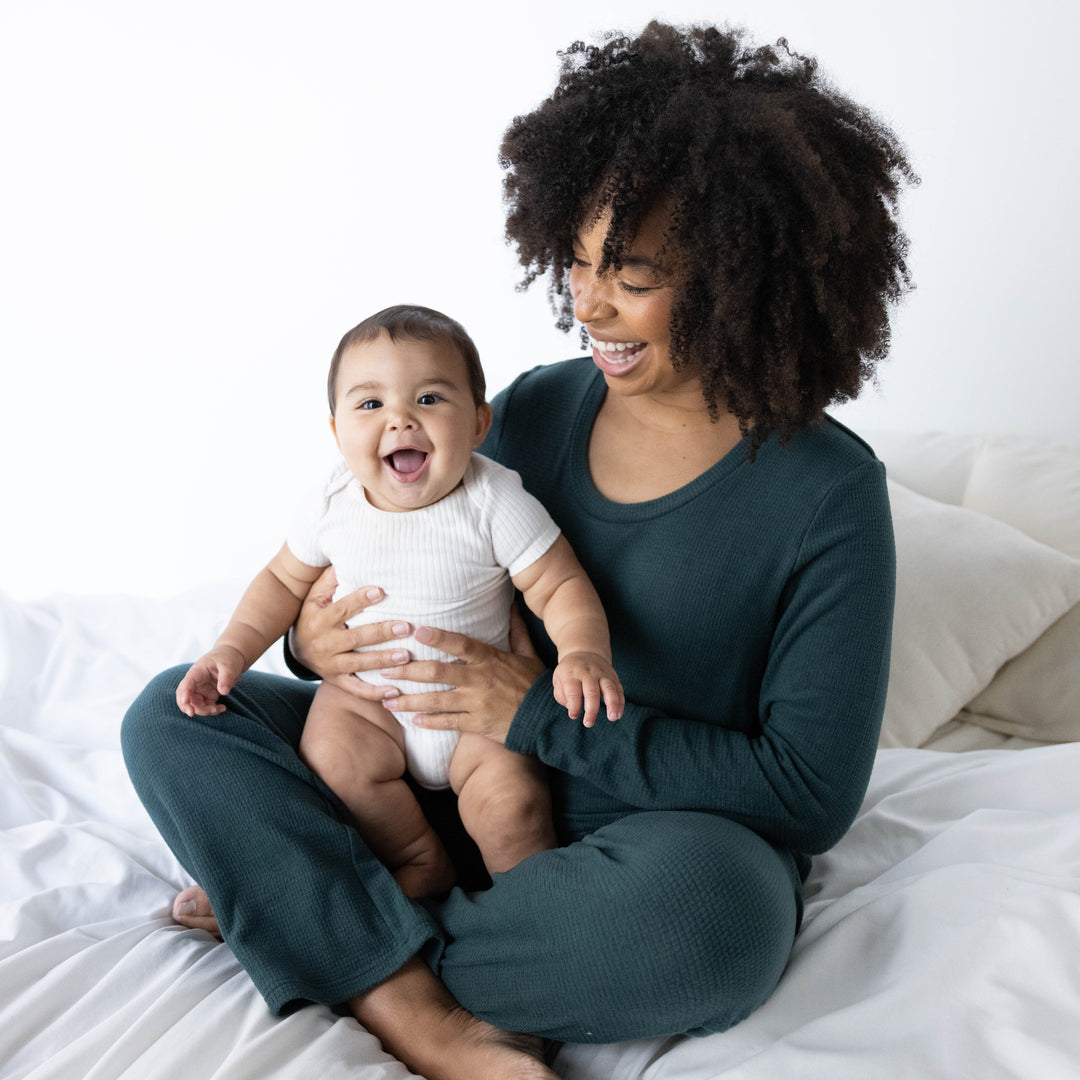 Model wearing the Fleece Nursing & Maternity Pajama Set in Evergreen with her baby in her lap. 