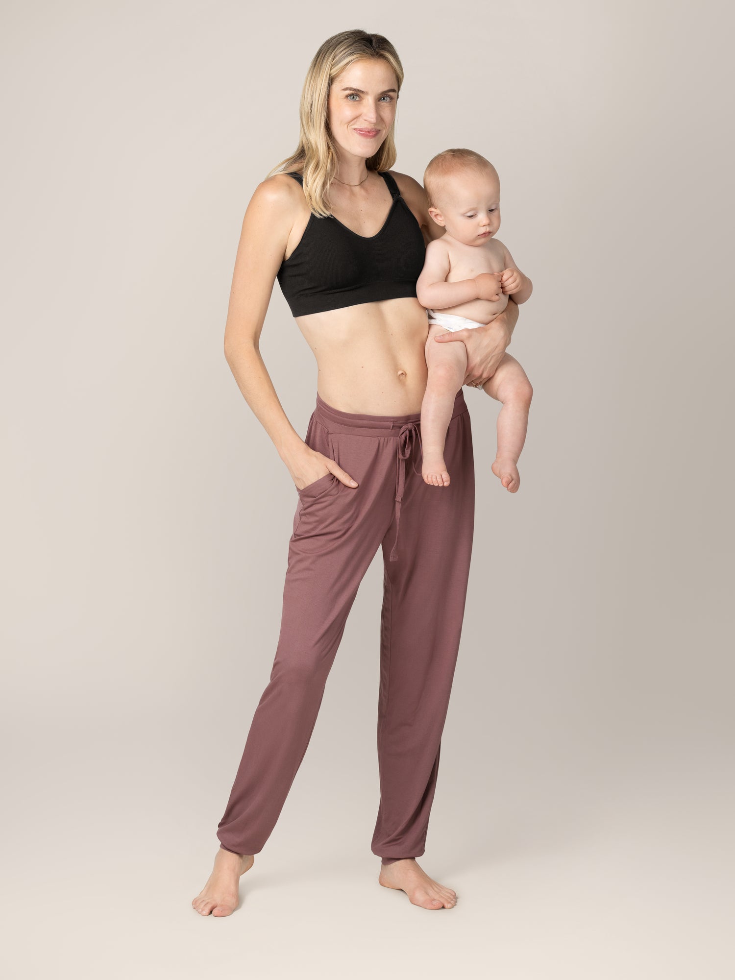 Model wearing the Mia Maternity & Nursing Lounge Bra in Black, paired with the Everyday Lounge Joggers in Twilight, and holding baby.