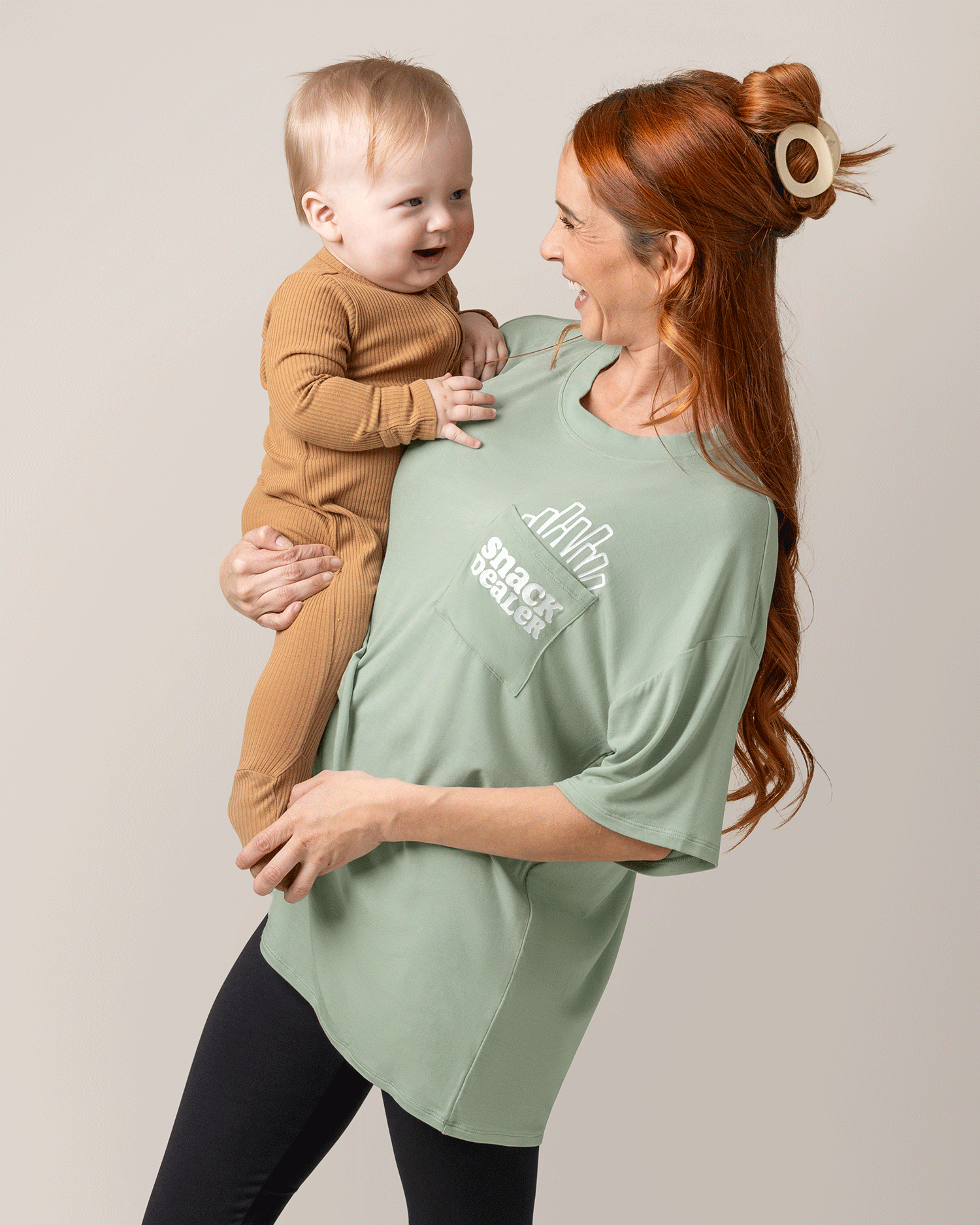 Front view of model wearing Oversized Graphic Tee in Snack Dealer, holding baby @model_info:Shannon is wearing a Small.