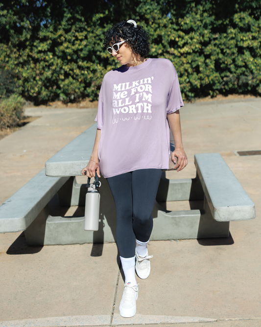 Model leaning against table outside and wearing the Oversized Graphic Tee in For All I'm Worth, paired with Louisa Legging @model_info:Indira is wearing an X-Large