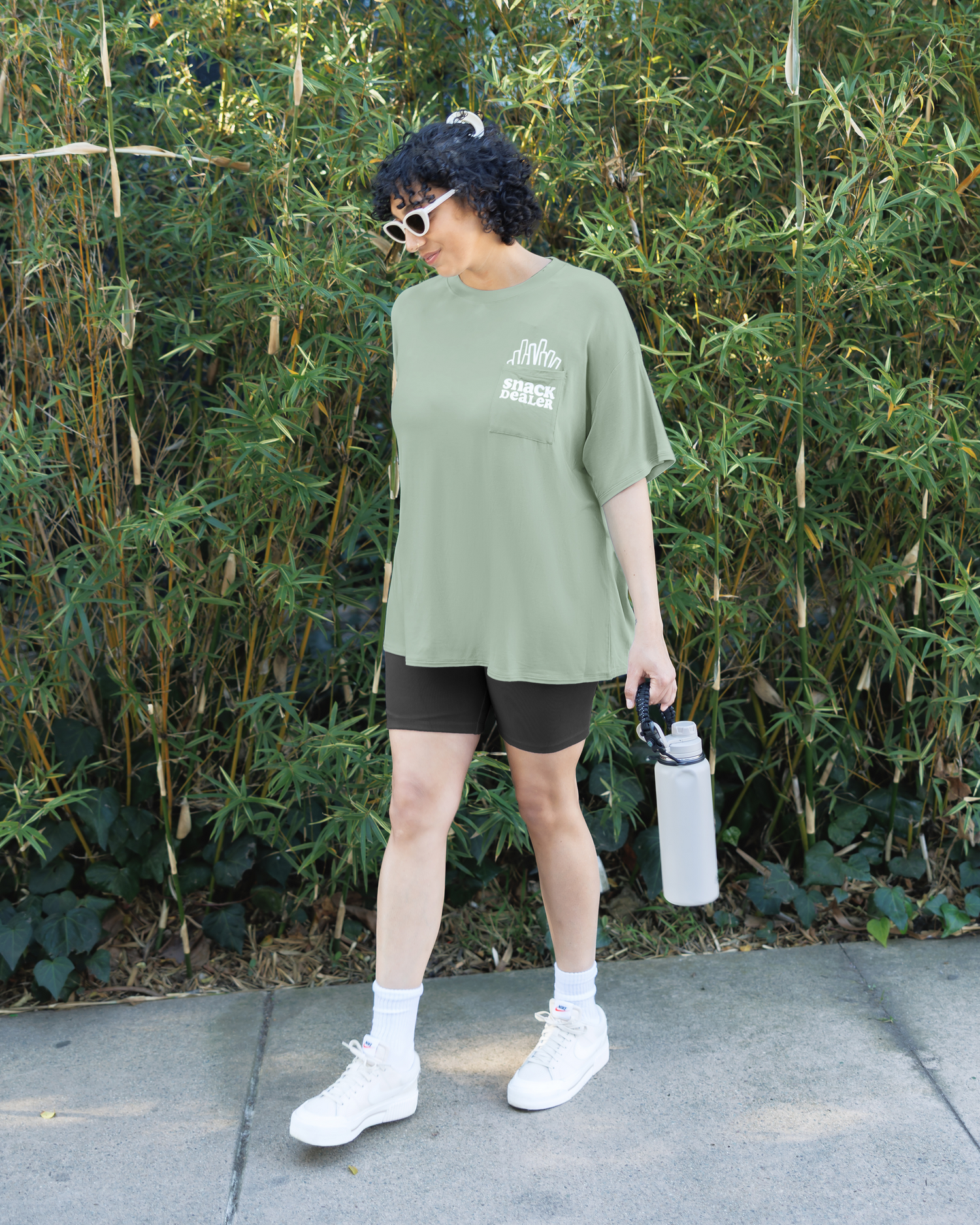 Model outside wearing Oversized Graphic Tee in Snack Dealer, paired with Stevie Bike Short@model_info:Indira is wearing an X-Large.