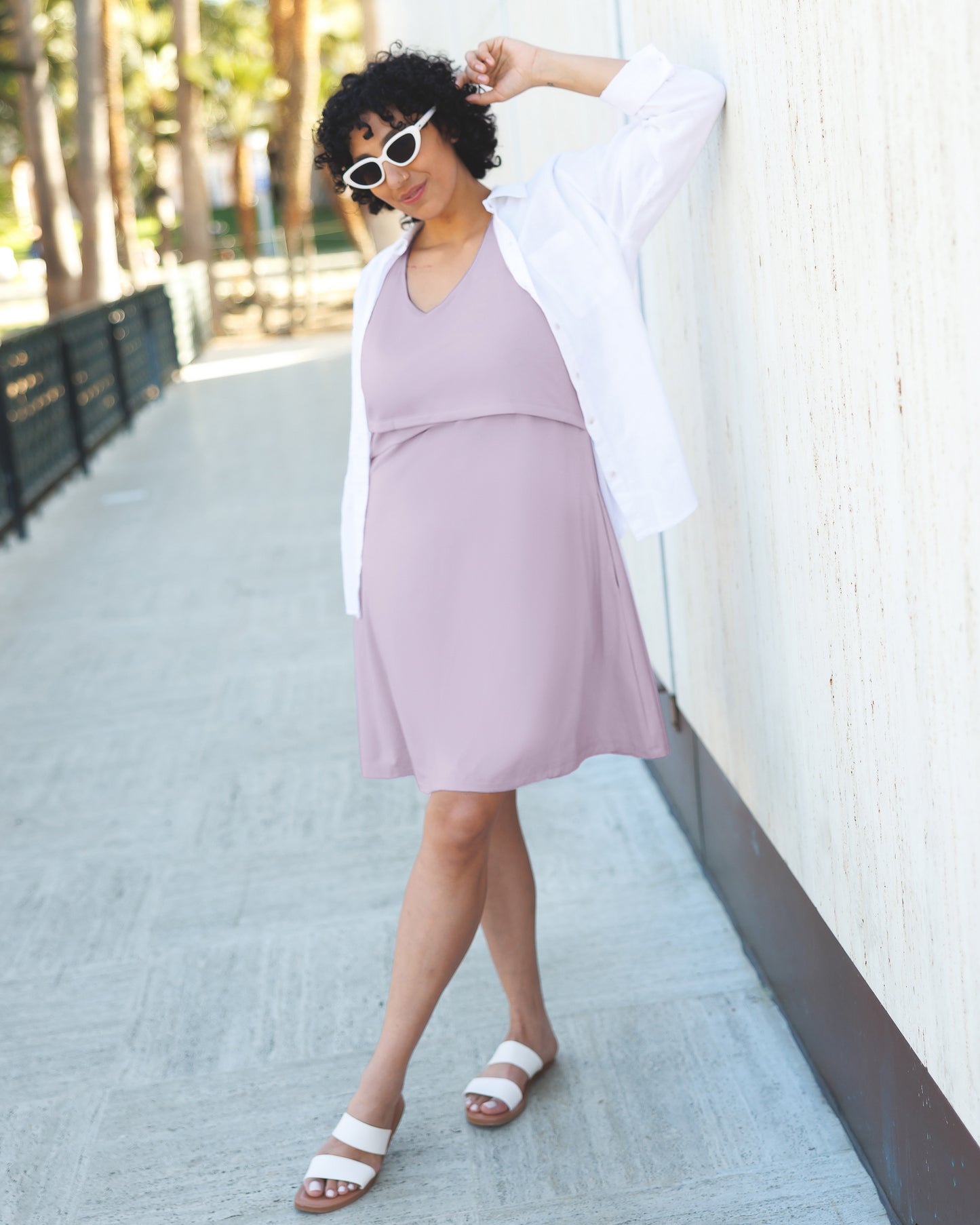 Model outside wearing the Penelope Crossover Nursing Dress in Lavender Mist, paired with an open white button down shirt and sandals