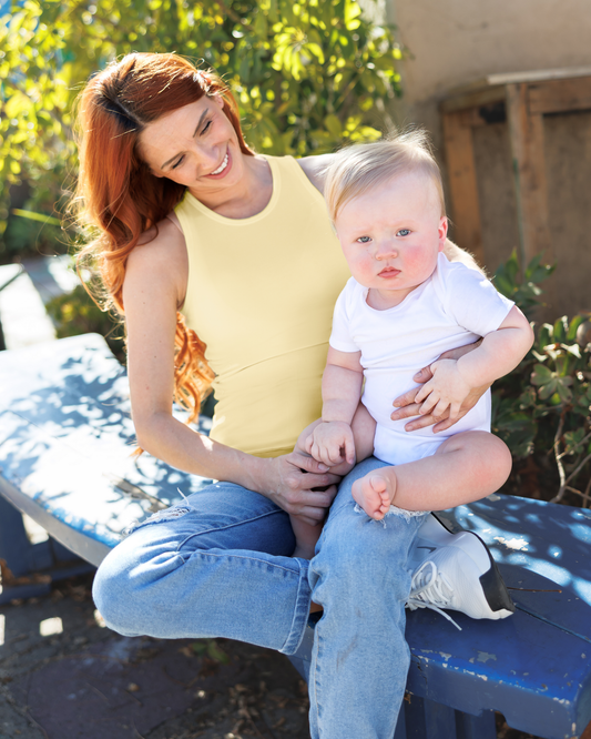 Model sitting outside holding baby wearing the Ribbed Bamboo Racerback Nursing Tank in Butter Yellow, paired with jeans@model_info:Shannon is wearing a Small