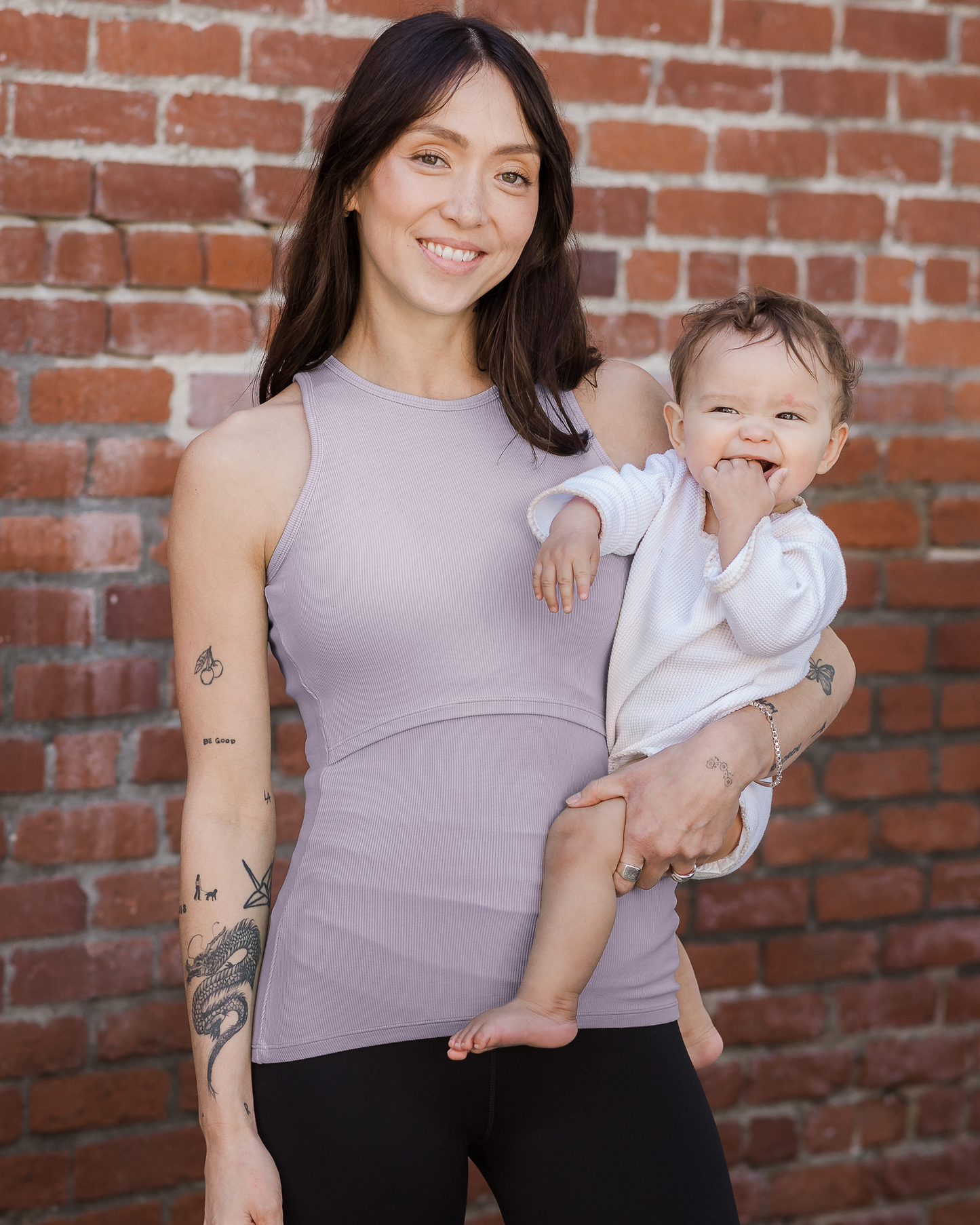 Model outside holding baby wearing the Ribbed Bamboo Racerback Nursing Tank in Lavender Mist@model_info:Lyn is wearing a Small.