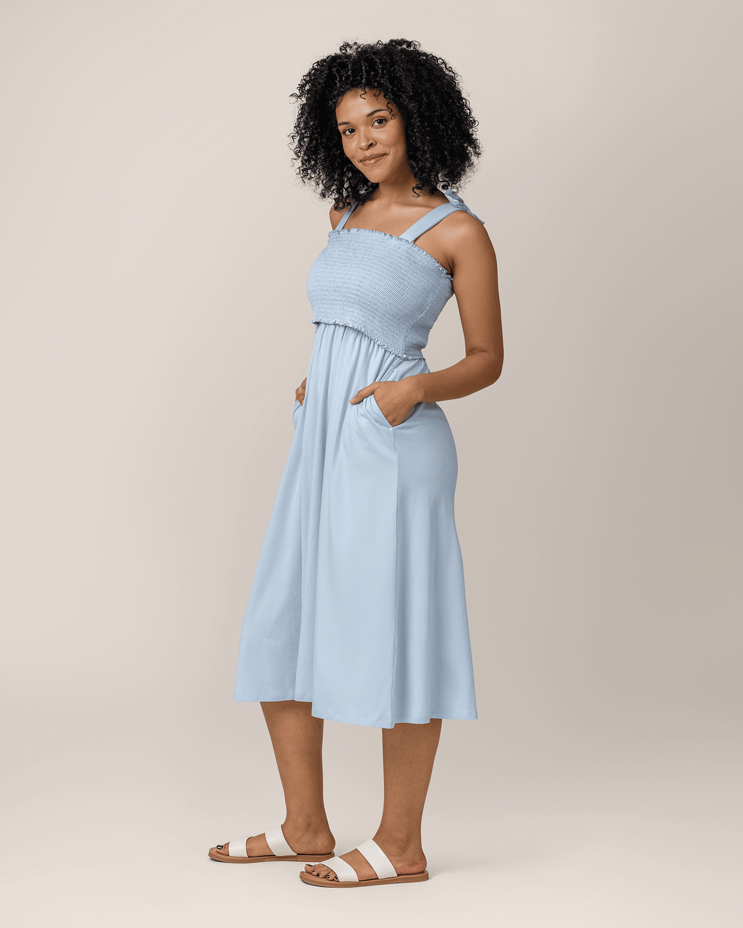 Side view of model wearing the Sienna Smocked Maternity & Nursing Dress in French Blue, with hands in pockets