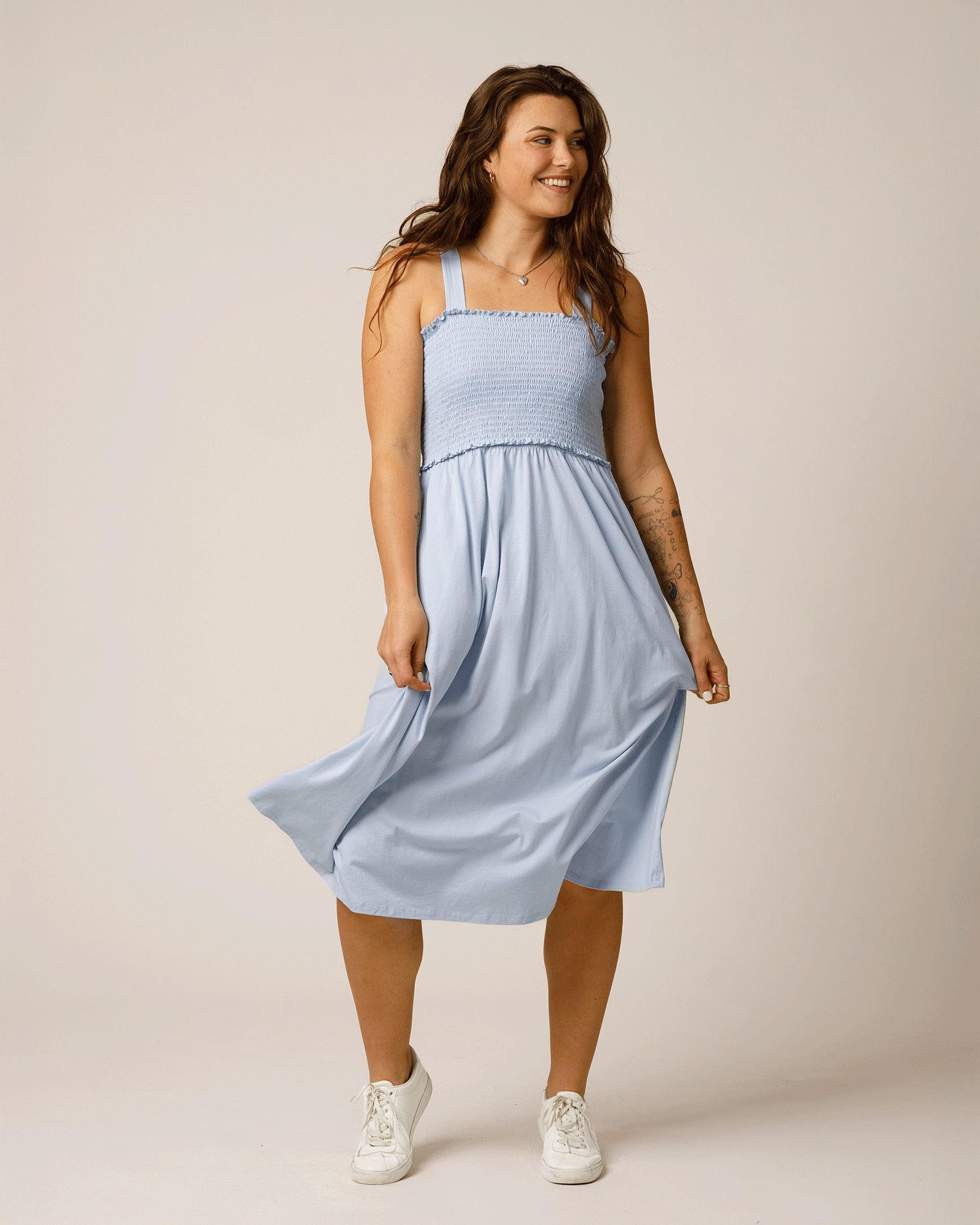 Front view of model wearing the Sienna Smocked Maternity & Nursing Dress in French Blue, showing flow of the skirt, paired with white tennis shoes @model_info:Gibson is 5'9" and wearing a Medium.