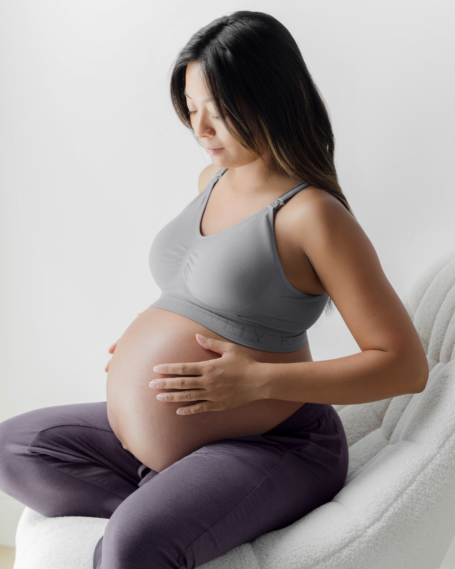 Pregnant model wearing the Simply Sublime® Nursing Bra in grey, sitting on chair