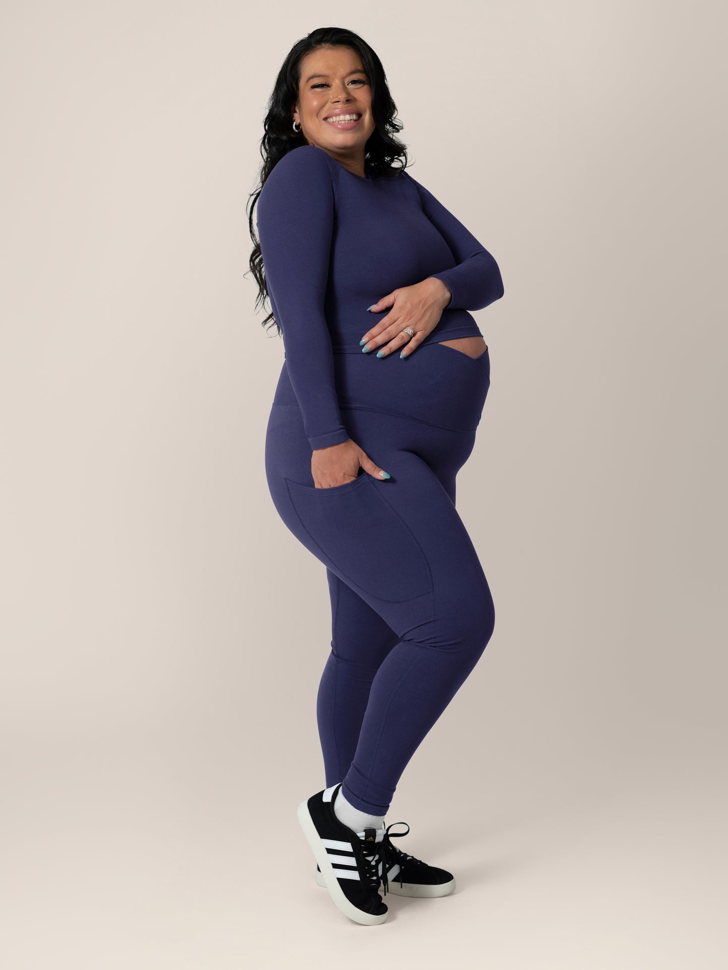 Side view of model wearing the Sublime®️ Bamboo Maternity & Postpartum Crossover Legging in Navy, with one hand in pocket, paired with matching Sublime® Bamboo Maternity & Nursing Cropped Long Sleeve Top. @model_info:Christina is 5'3" and wearing a Large.