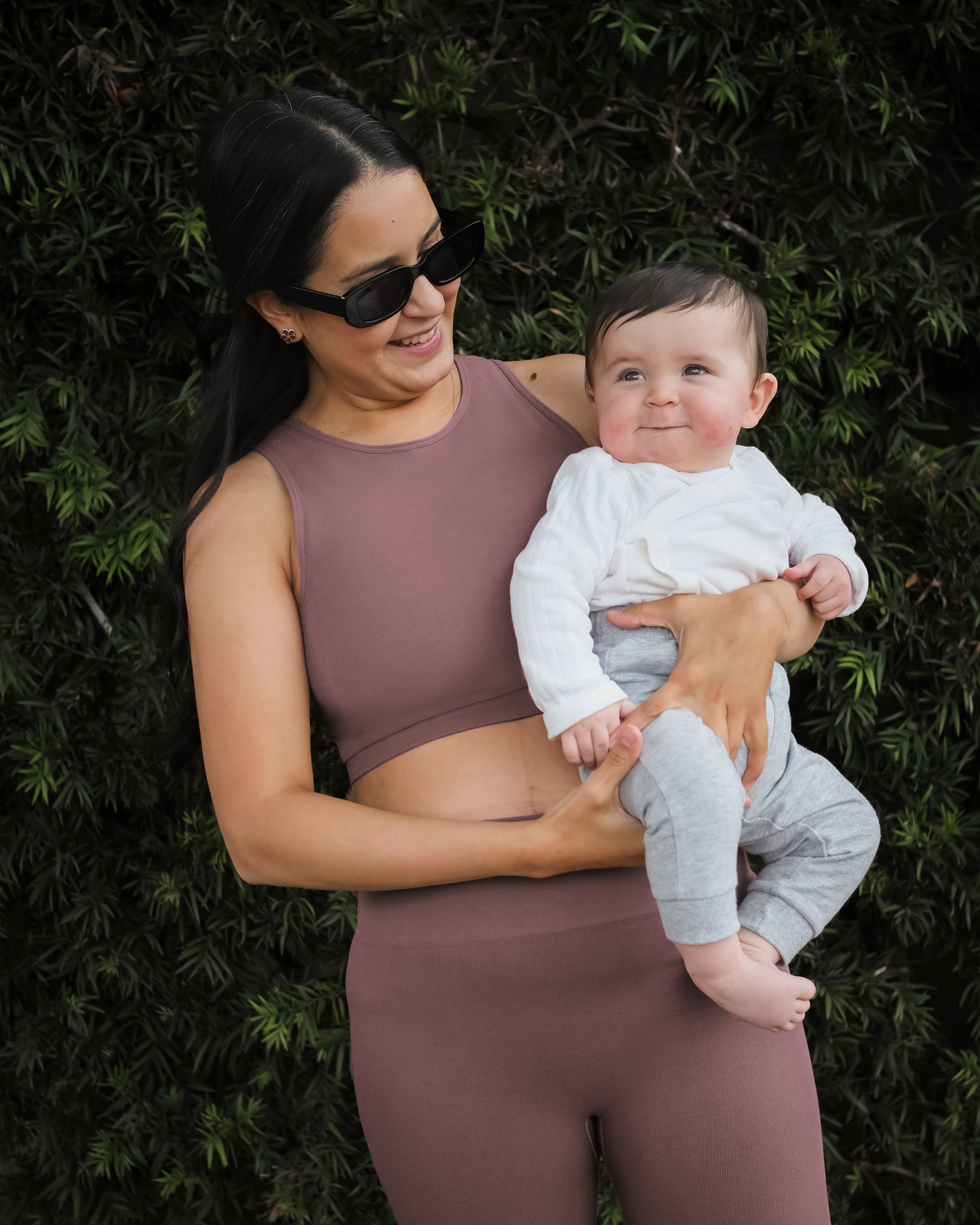 Model holding baby outside wearing the Sublime® Bamboo Hands-Free Pumping Longline Bra Top in Twilight, paired with matching Sublime® Bamboo Maternity & Postpartum Bike Short