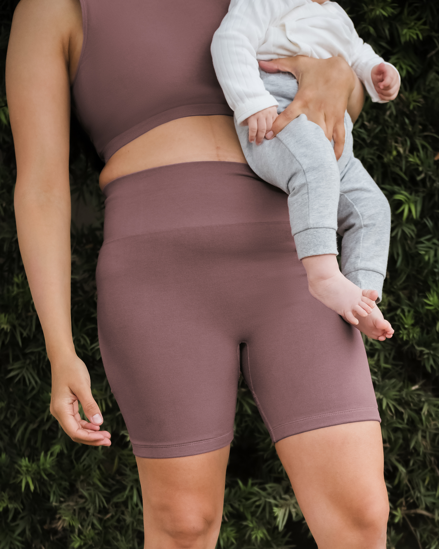 Cropped in image of model outside holding baby and wearing the Sublime® Bamboo Maternity & Postpartum Bike Short in Twilight paired with matching Sublime® Bamboo Hands-Free Pumping Longline Bra Top