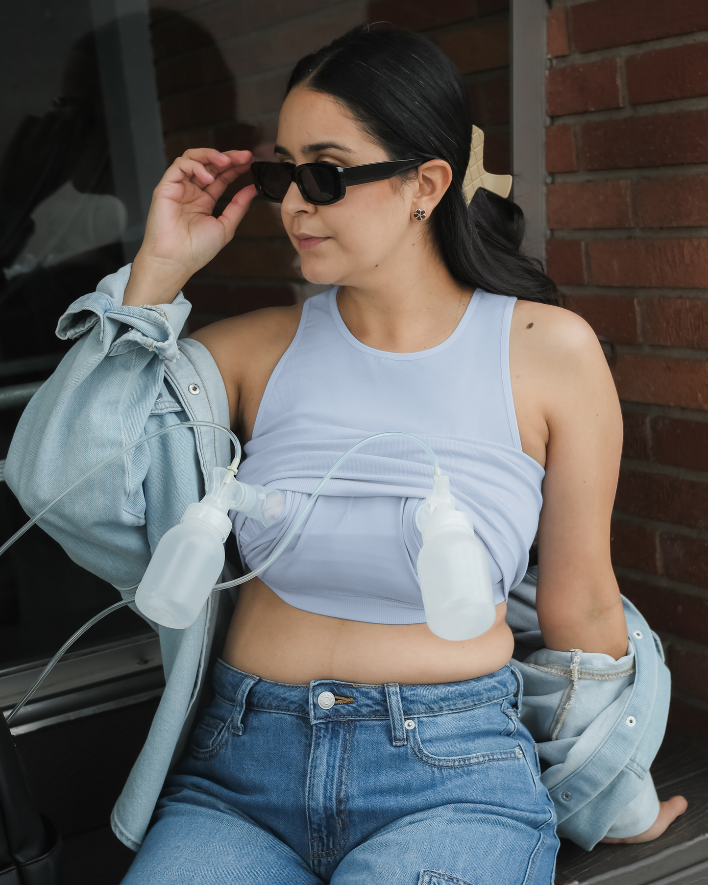 Model sitting outside wearing the Sublime® Bamboo Hands-Free Pumping Longline Bra Top in French Blue, and pumping; paired with jeans and a slouched open button-down top @model_info:Dama is wearing a Medium Busty.