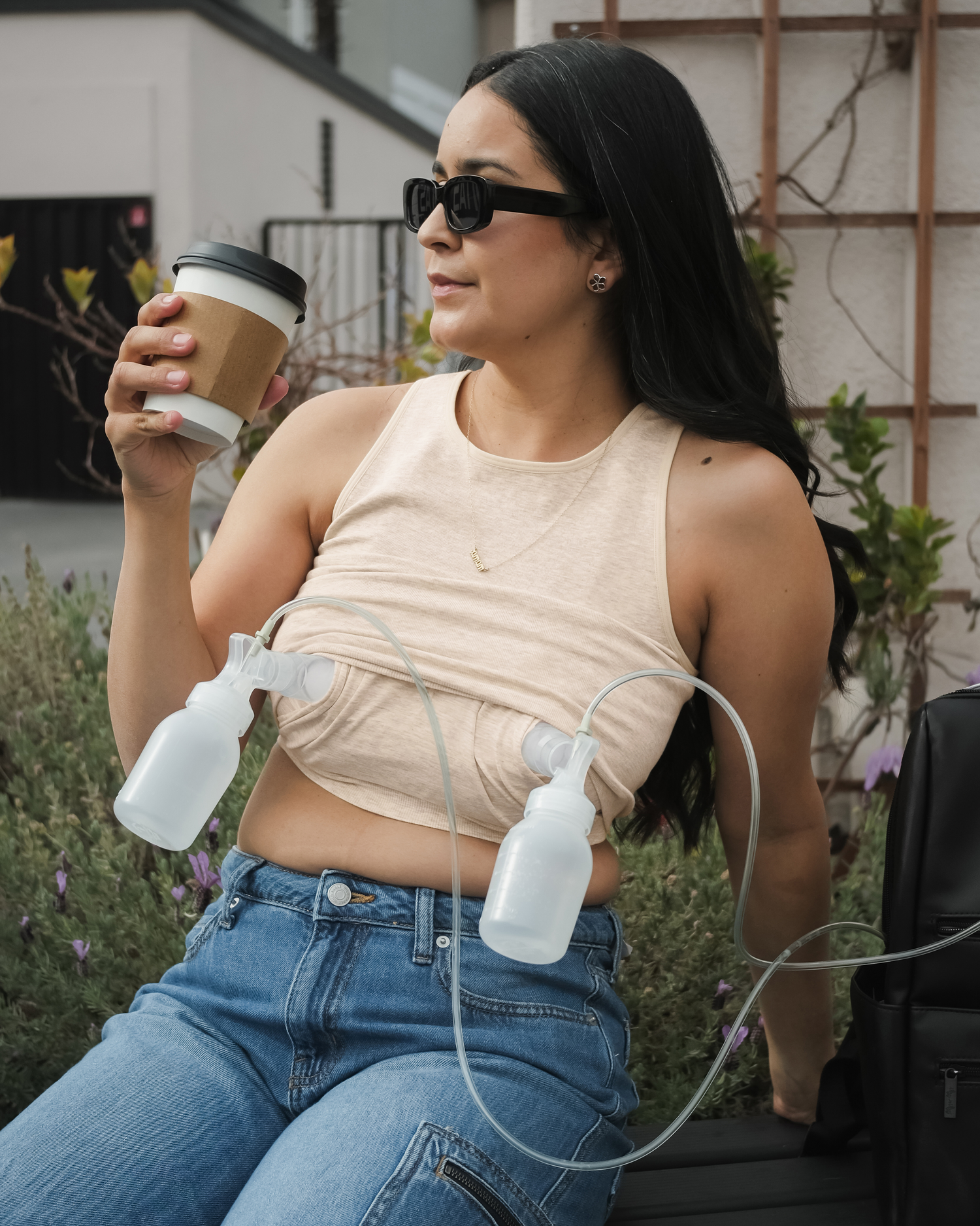 Model sitting outside wearing the Sublime® Bamboo Hands-Free Pumping Longline Bra Top in Oatmeal Heather, pumping hands-free while drinking coffee