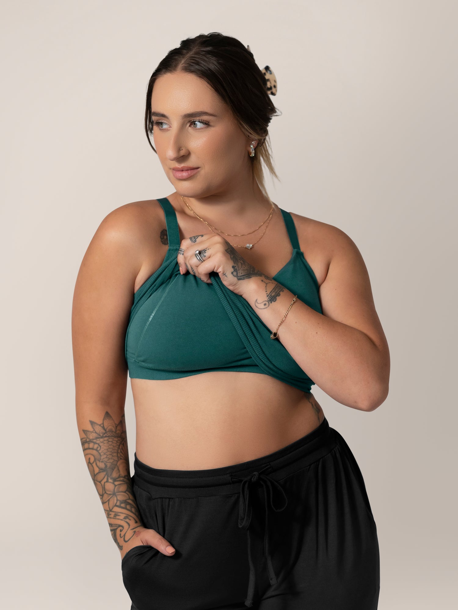 Front view of model wearing the Sublime® Bamboo Hands-Free Pumping Lounge & Sleep Bra in Evergreen, lifting outer layer to show pumping access.