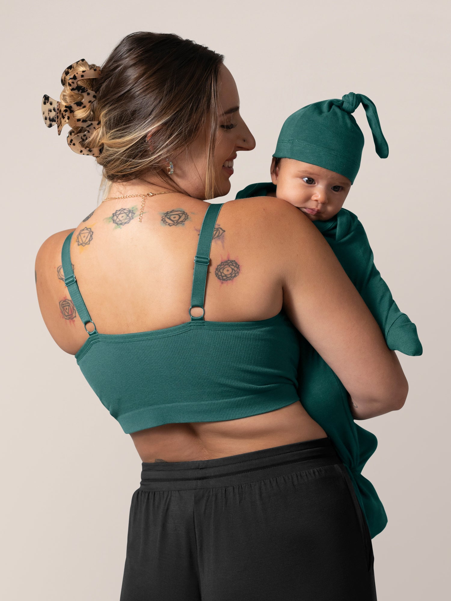 Back view of model wearing the Sublime® Bamboo Hands-Free Pumping Lounge & Sleep Bra in Evergreen, holding baby.