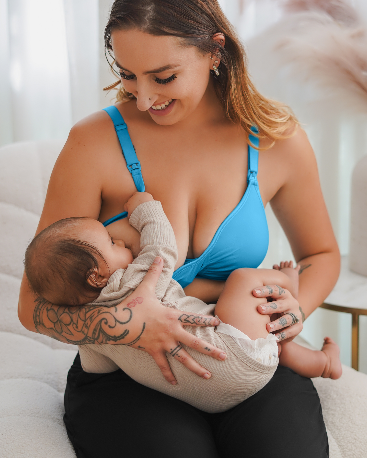 Model sitting wearing the Tatum Seamless Maternity & Nursing Bralette in Blue Lagoon, and nursing baby