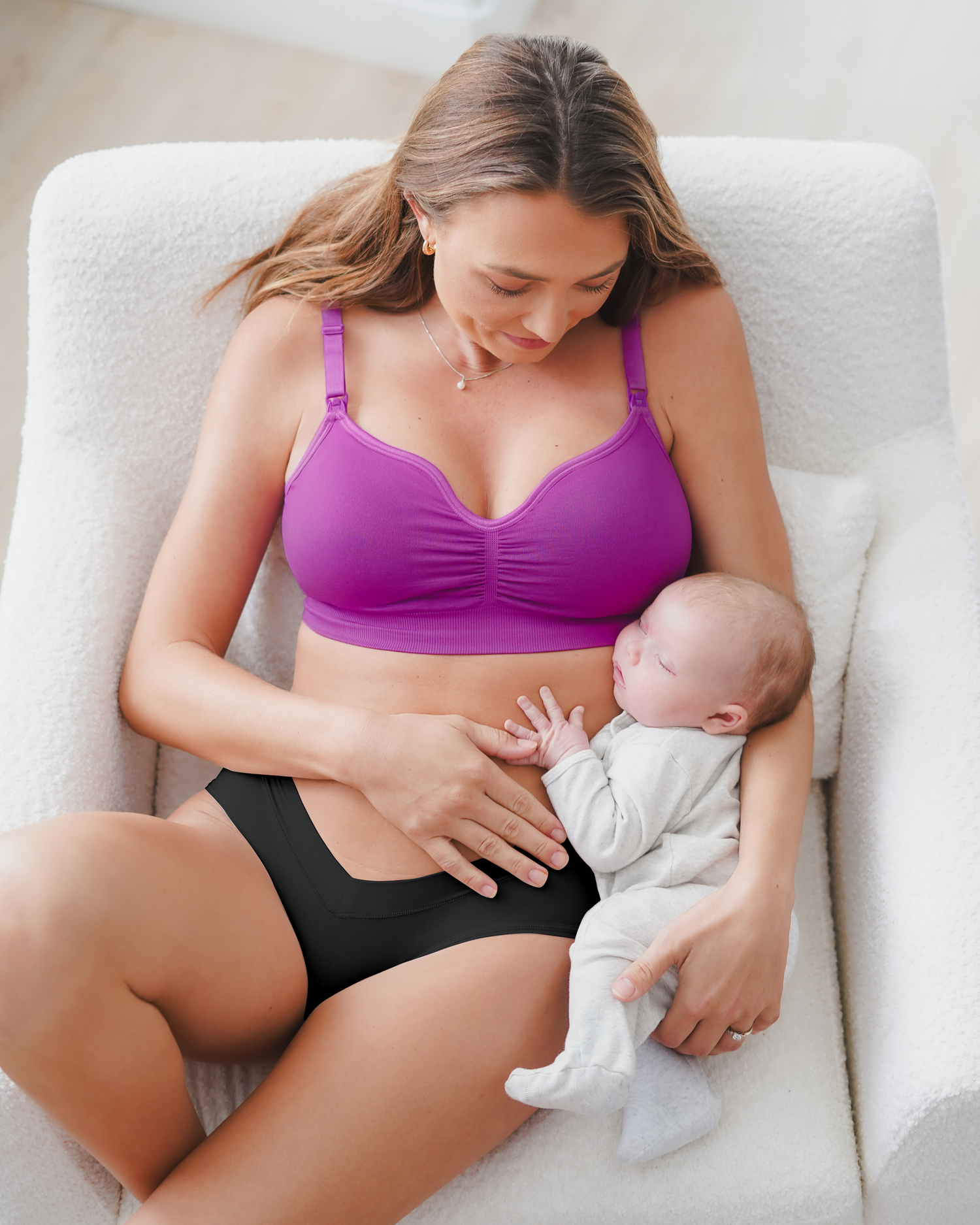 Model lounging on chair with baby wearing the Tatum Seamless Maternity & Nursing Bralette in Orchid. @model_info:Kate is wearing a Small.