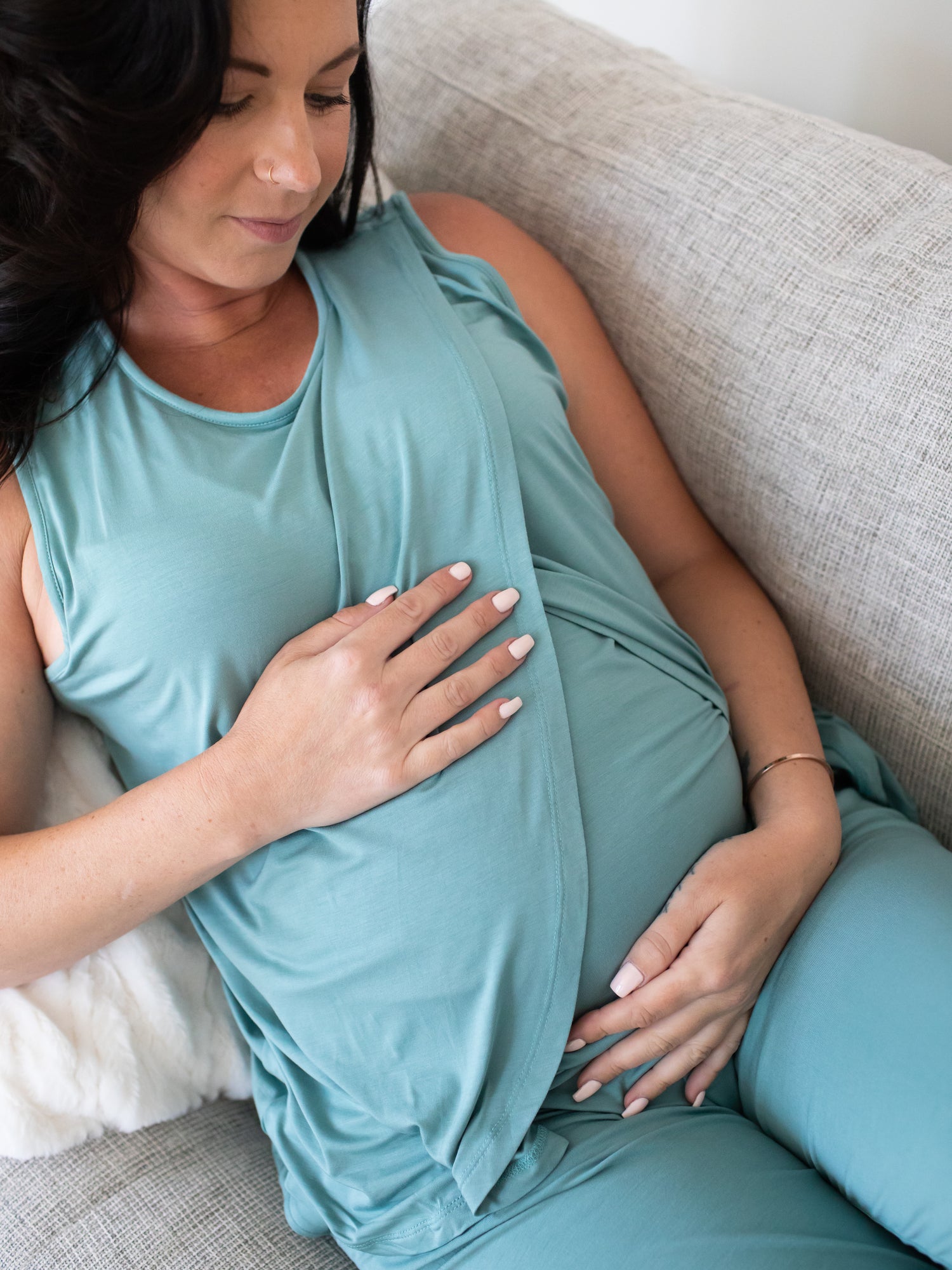 Cropped in view of pregnant model sitting cross-legged on bed wearing the Tulip Hem Nursing Tank & Capri Pajama Set in Aqua showing crossover of fabric on the top