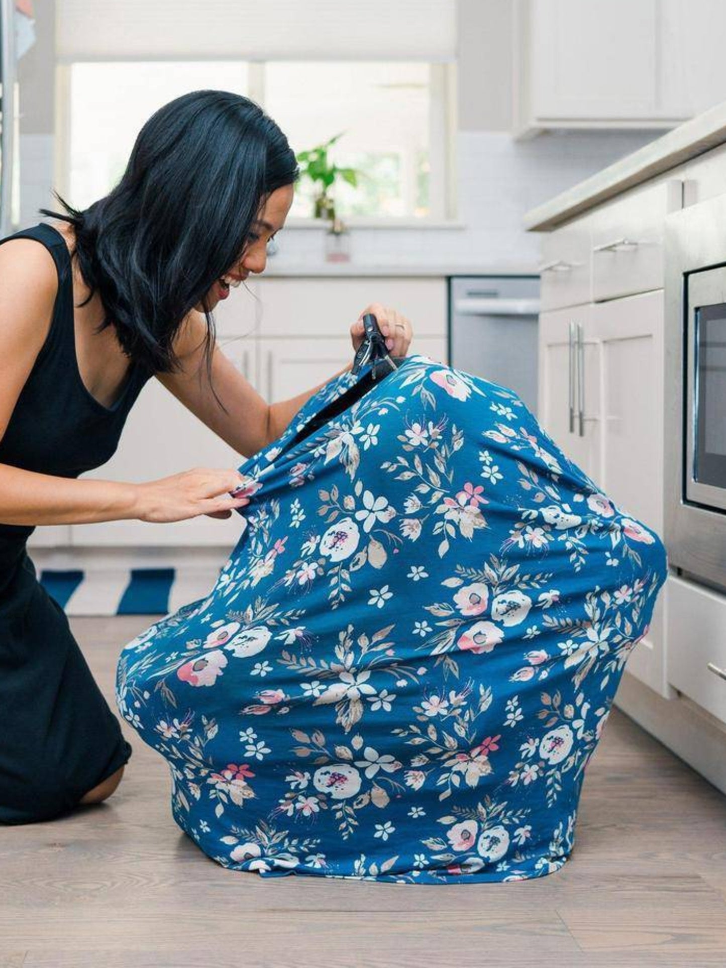 The Bebe au Lait - 5-in-1 Multi-Use Nursing Cover in Midnight Floral being used as a carseat cover, with mom peeking in on baby